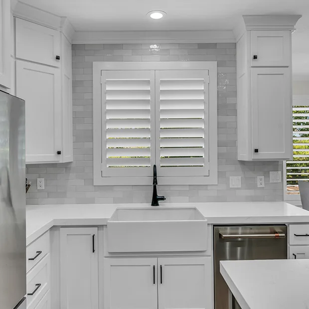 White Polywood shutters on a kitchen window over the sink and on a window in the background in a dining area
