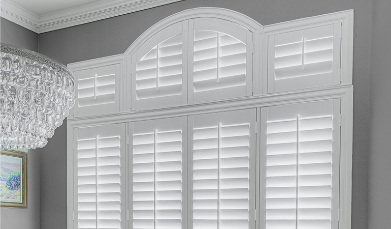 White Polywood shutters on an arched window in a formal dining room.