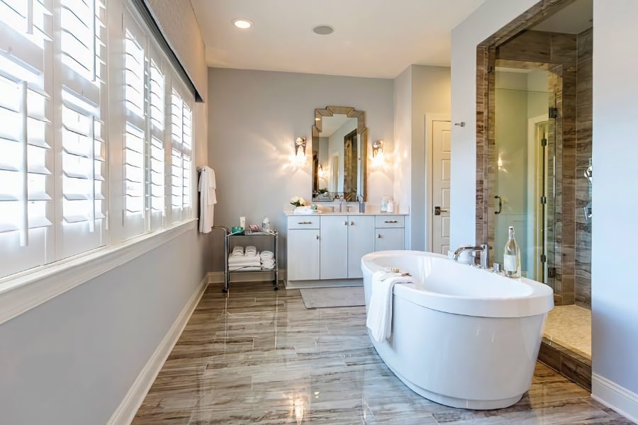 The flooring in this modern bathroom contrasts nicely with the neutral walls and white plantation shutters. Stylish bathroom with plantation shutters, distinctive flooring, and free-standing tub.