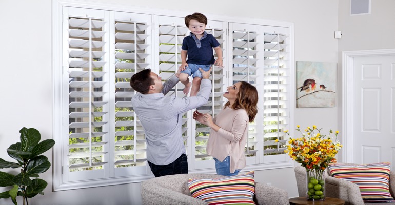 Your kids need a window treatment that holds up to their endless energy. Parents Lifting Child In Front of Window Treatments