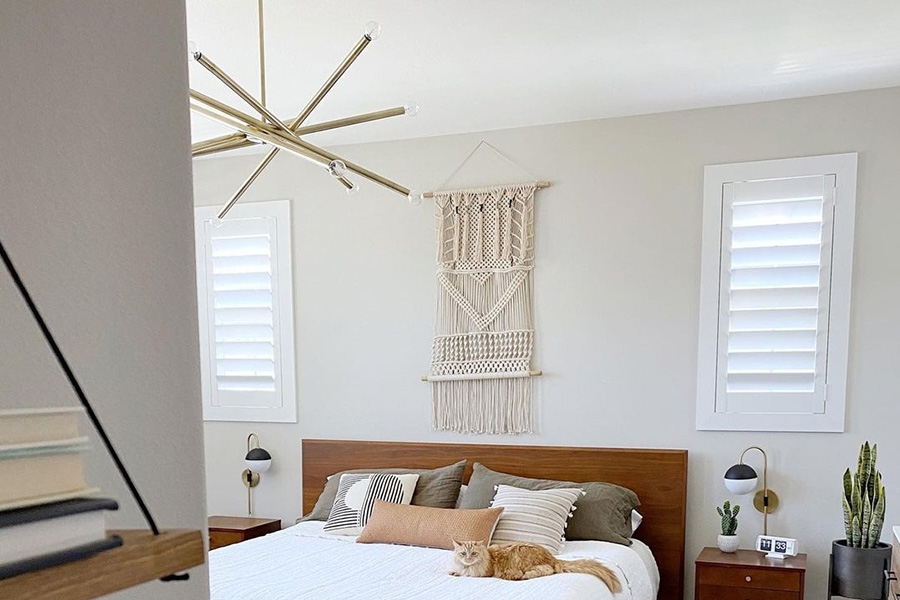 Durable Polywood shutters are a must-have for any pet owner. White Polywood shutters in a bedroom with two cats climbing on the bed