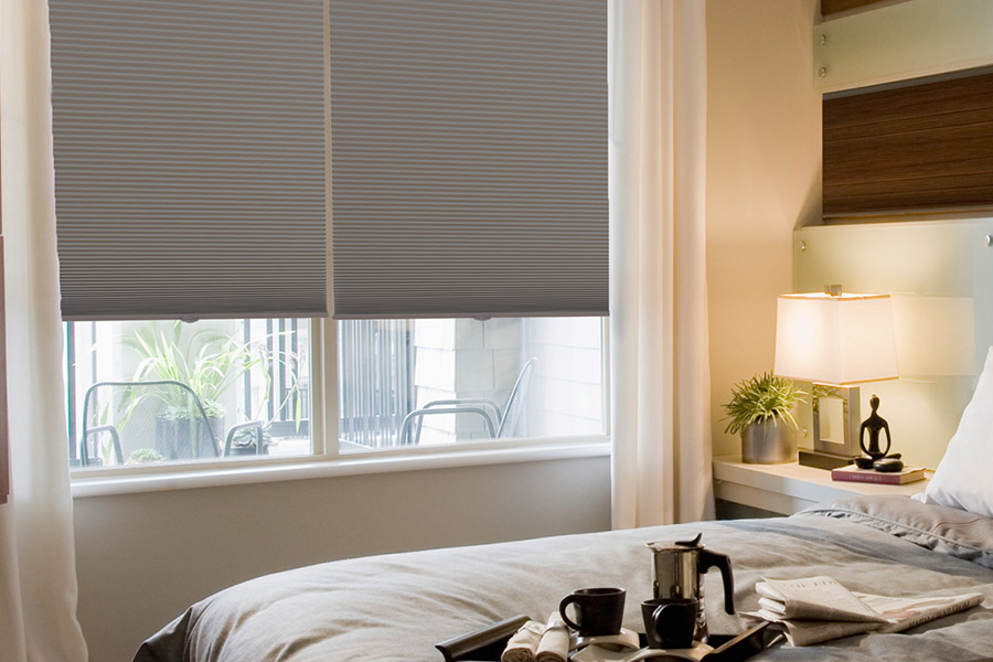 Create a cozy atmosphere with energy-efficient cellular shades in your bedroom. Gray cellular shades on bedroom windows