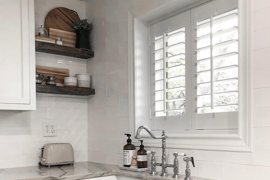 Moisture-resistant Polywood shutters are the best window treatments for a kitchen. Photo Credit: Sincerely McCraw  White and sleek kitchen with Polywood shutters above a kitchen sink.