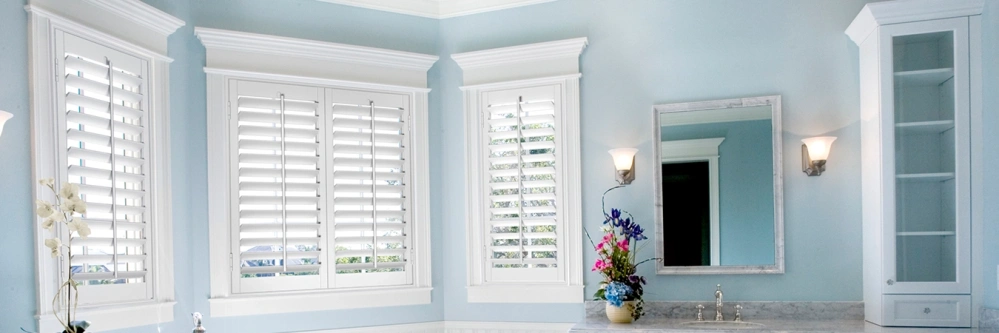White Polywood shutters on windows in a blue bathroom