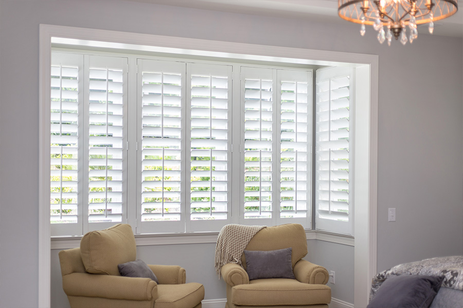 Tidy up your window trim with a fresh coat of paint. White Polywood shutters in a sitting area of a bedroom.