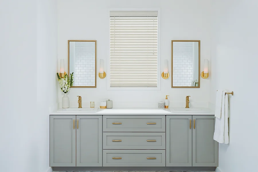 Duarble, water-resistant faux-wood blinds are perfect for bathrooms. White faux-wood window blind in a white bathroom with a grey double vanity